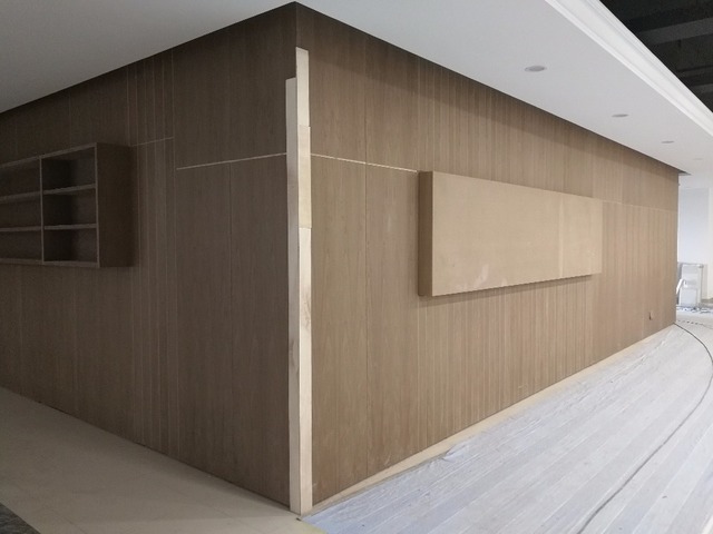 Modern office space designed by Funlink Creative Sdn Bhd, featuring a sleek wooden panel wall with built-in shelves, creating a warm, minimalist aesthetic. The light wood tones complement the soft grey flooring, balancing functionality and style. Perfect for a trendy workplace renovation.