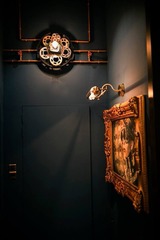 This image, by BANGKU STORE, showcases a corner of the HUGO STEAMPUNK PREMIUM LOUNGE with a steampunk aesthetic. A dark blue wall serves as the backdrop for a vintage gold-framed painting, illuminated by an antique-inspired sconce. Copper pipes add an industrial touch, complementing the pseudo-Victorian era's mechanical charm. This Malaysian interior design masterpiece melds historical elegance with a bold visionary twist ideal for steampunk enthusiasts and design aficionados.