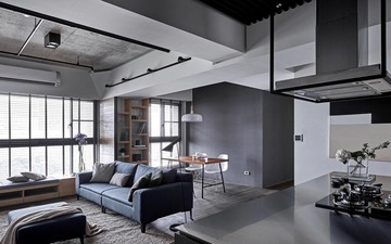 This image showcases a condo living room interior designed by KAIU Concept & Construction Sdn. Bhd., featuring a contemporary industrial theme. The raw, textured grey walls and ceiling ducts are complemented by sleek metal accents and wood elements. Charcoal and slate hues dominate, punctuated by a navy blue sofa and warm wood-toned furniture. Natural light filters through the horizontal blinds, highlighting the minimalist aesthetic and modern charm characteristic of industrial design for condos.