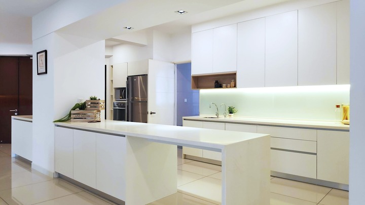 This sleek kitchen from R Works' 9 Bukit Utama Condominium portfolio exudes minimalist modernity, emphasizing functionality within a spacious design. The clean lines of the white cabinetry offer abundant storage, complemented by a chic central island. Soft lighting enhances the serenity, highlighting the room's spotless aesthetic, perfect for interior design enthusiasts seeking inspiration for a tidy, contemporary home space.