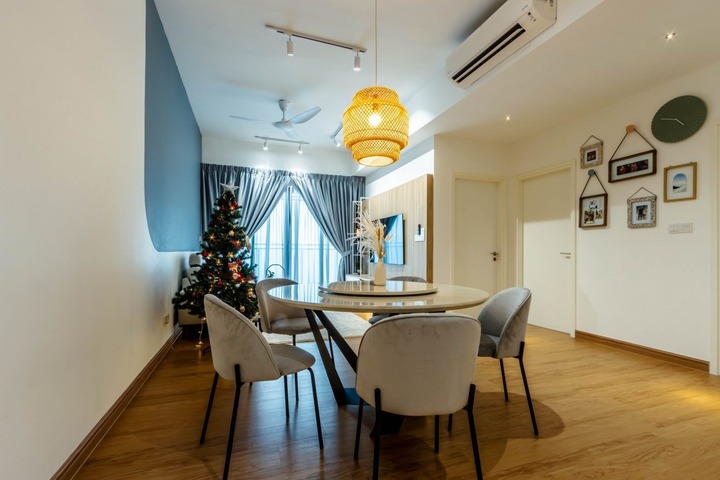 Scandinavian-themed dining area by R Works at Seventeen Residences, Seksyen 17, showcasing a sleek white and blue color palette. A round dining table with comfortable gray chairs is the focal point, illuminated by a statement geometric light fixture. The space is defined by clean lines and a minimalist aesthetic, with natural light streaming through sheer curtains, accented by a festive Christmas tree and stylish wall art, demonstrating the firm's commitment to cozy, yet contemporary, interior design.