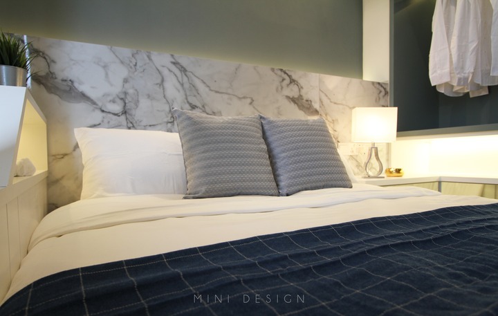 This stylish bedroom, featured by Mini Design, showcases a contemporary approach to modern design in a 1200sf Penang condo. The space has a chic marble headboard complementing the serene grey and white color scheme, accented by a bold navy bedspread. Streamlined furnishings and subtle lighting contribute to the room's elegant, sophisticated ambiance, epitomizing Mini Design's sleek, modern aesthetic.