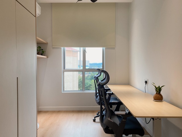 Reflecting the Japandi style of 3STEPS DESIGN's RESTFUL HOME project, this interior showcases a minimalist home office with a slim, wooden desk paired with ergonomic black chairs. Warm daylight illuminates the space through a large window, highlighting the neutral color palette and clean lines. A small potted plant adds a touch of nature, complementing the functional yet serene ambiance perfect for peaceful productivity.